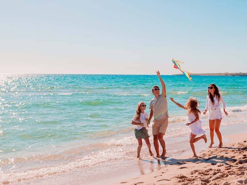 A family flying a kite and enjoying time on a sunny beach while on holiday.