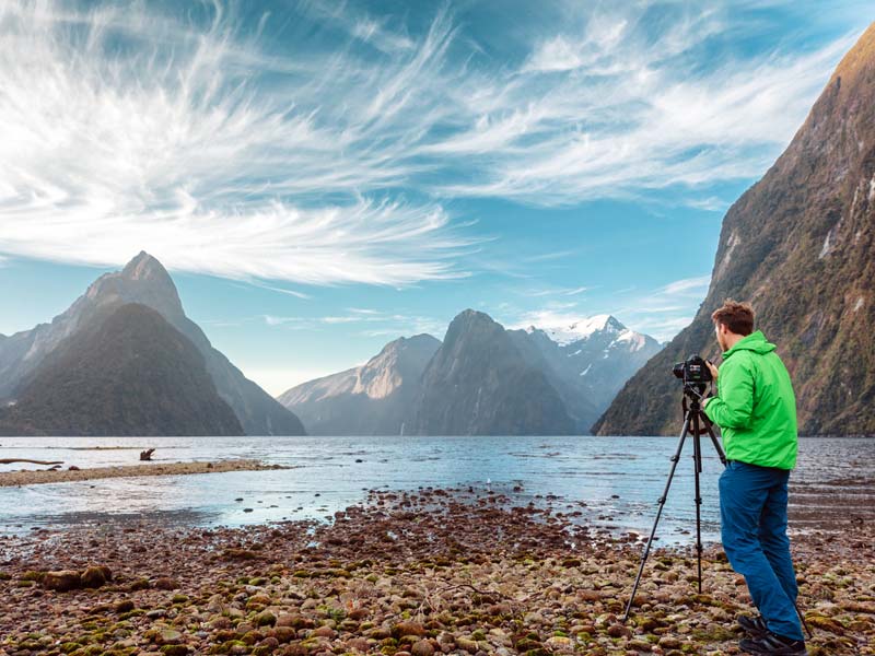 A tourist setting up a tripod to take a photograph of a mountain landscape.